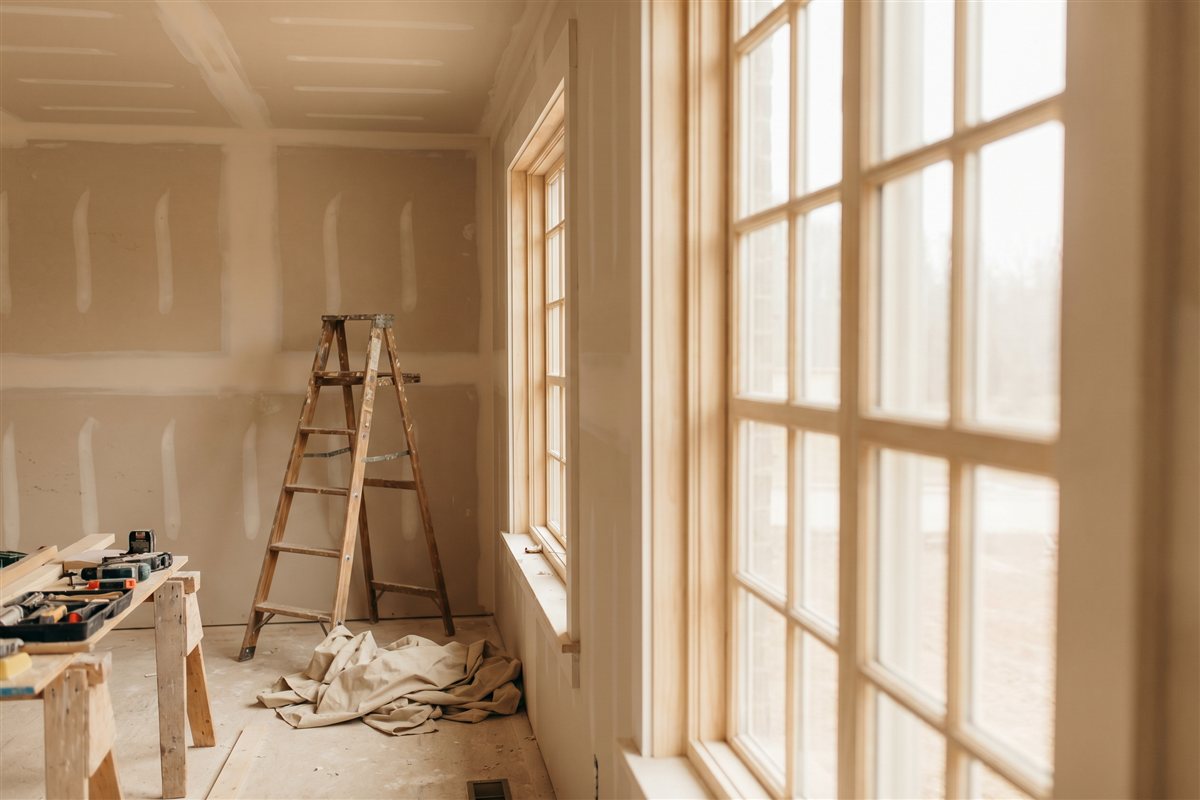 American home remodel in progress at the drywall stage with a step ladder and drop cloths