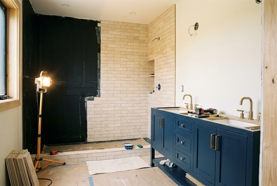 Canadian bathroom during fit-out showing tiling over a waterproofing membrane and a navy vanity with brushed brass taps
