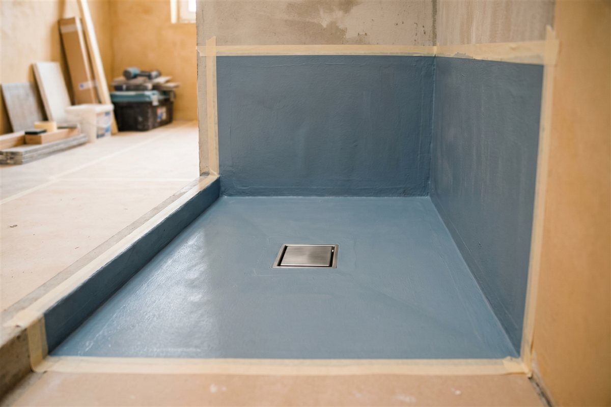 Bathroom walls and shower base with a blue-grey waterproofing membrane and floor drain before tiling
