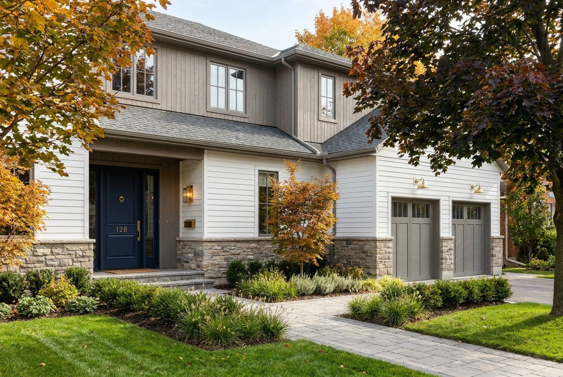 A fully renovated two-storey Canadian house exterior with warm white siding, a stone base, a navy front door with brass hardware, and mature autumn maples