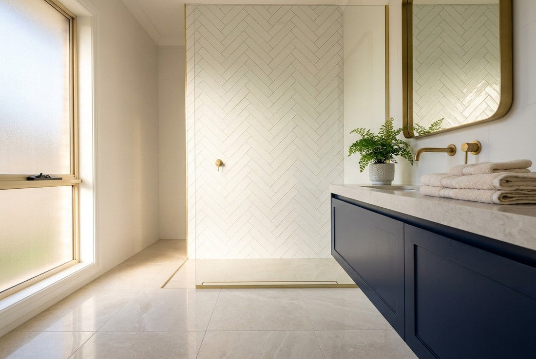 Freshly tiled Australian bathroom with herringbone feature wall, pale stone floor tiles, navy vanity and brass fixtures