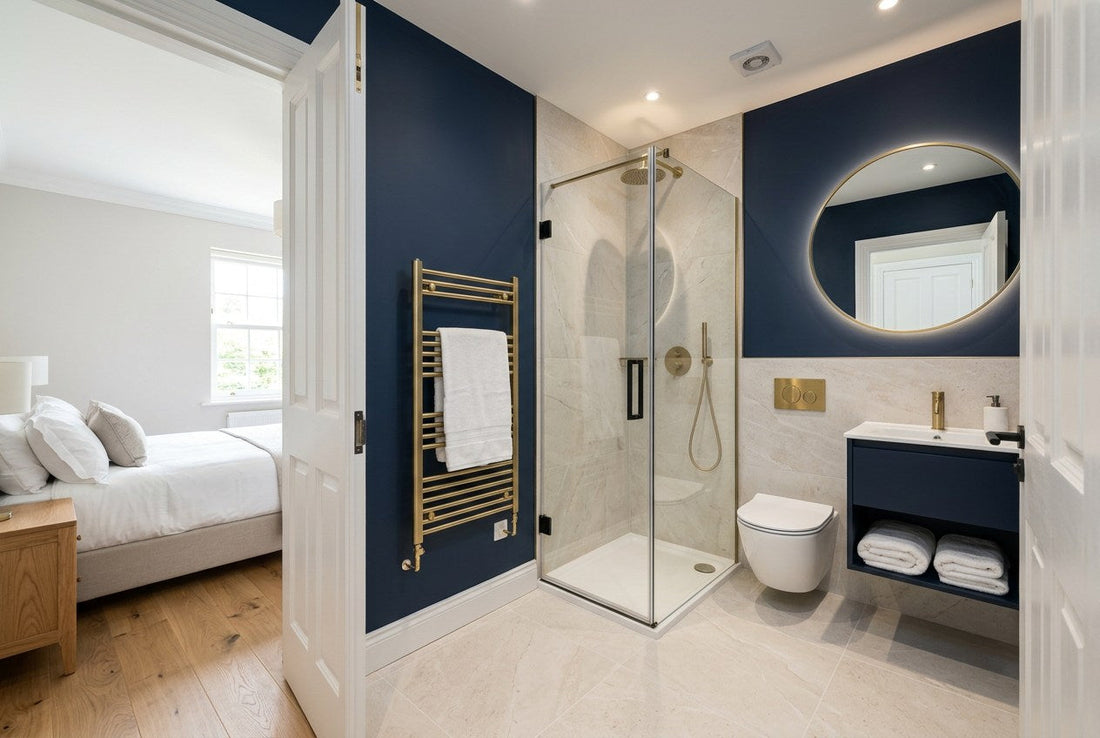 Finished compact Irish ensuite bathroom seen from the bedroom, with corner glass shower, wall-hung WC, navy vanity and brass fittings