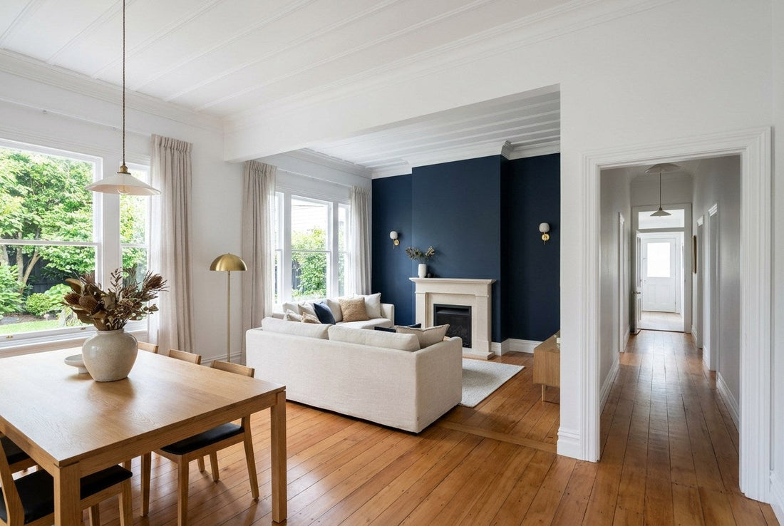 Finished New Zealand villa renovation with restored timber floors, navy feature wall, brass sconces and a styled open-plan living and dining space