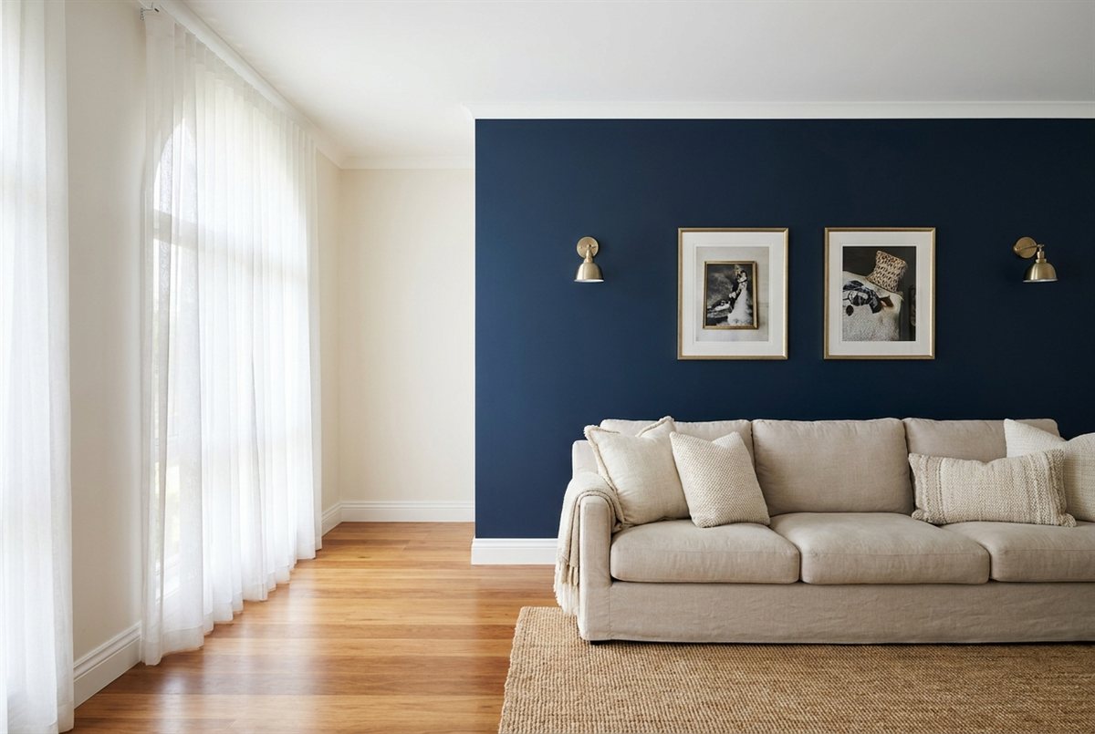 Freshly painted Australian living room with a deep navy feature wall, white ceiling and trim, brass sconces and a neutral sofa