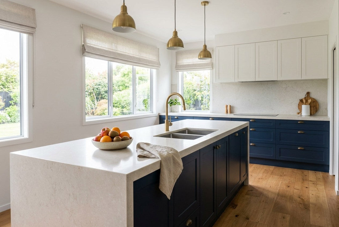 Finished New Zealand kitchen with a pale stone benchtop and waterfall island end, navy shaker cabinetry and brass tapware