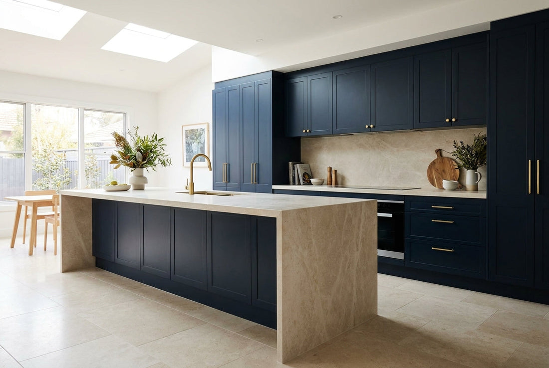 A renovated Australian kitchen with a large island, stone waterfall benchtop, navy cabinetry and brass tapware