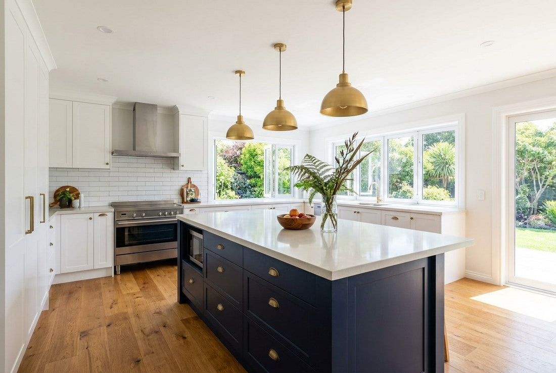 Fully renovated open-plan New Zealand kitchen with navy island, pale stone benchtop, white cabinetry and brass pendant lights