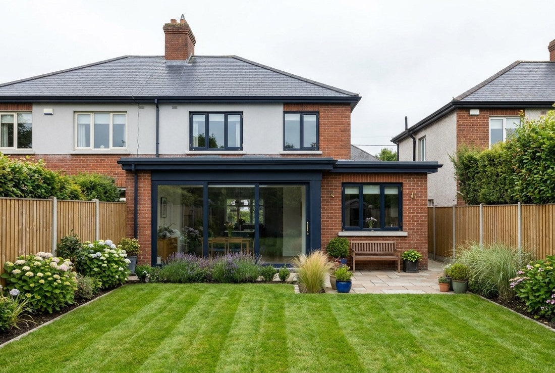 Rear exterior of a finished Irish semi-detached house with a modern single-storey rear extension, glazed sliding doors with navy frames and brass hardware, and a neat striped lawn under overcast Irish daylight
