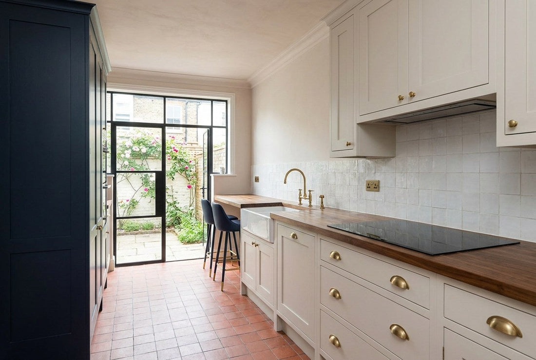 A completed kitchen in a renovated UK Victorian terraced house, with pale in-frame cabinetry, a walnut worktop, an induction hob, brass fittings and a terracotta quarry-tiled floor