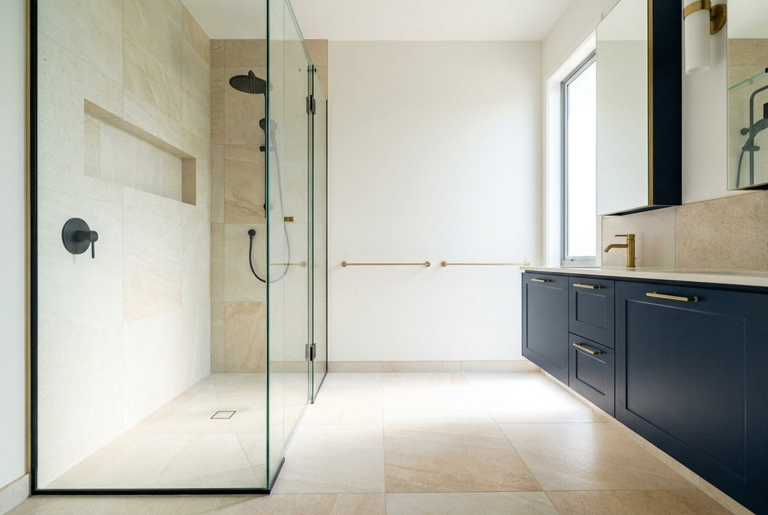 Fully finished frameless walk-in shower in a New Zealand bathroom renovation, waterproofed to E3/AS1 with pale stone tile, navy vanity, and brass fittings