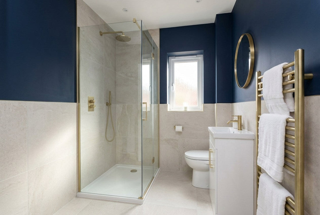 Renovated small British bathroom with navy walls, brass fittings, pale stone tiles and a glass shower enclosure