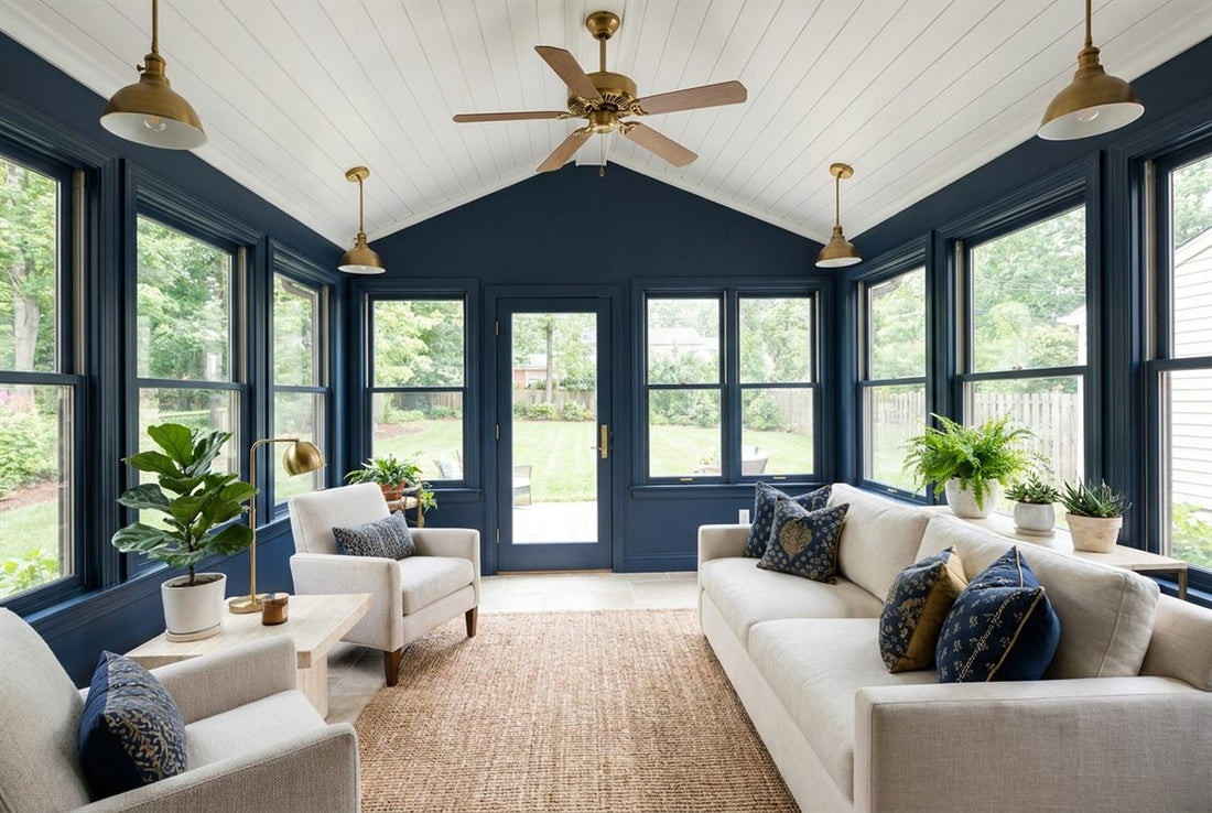 Fully finished four-season sunroom addition in a US home with navy accent walls, brass pendant lighting, a pale stone tile floor and a wall of windows onto a green backyard